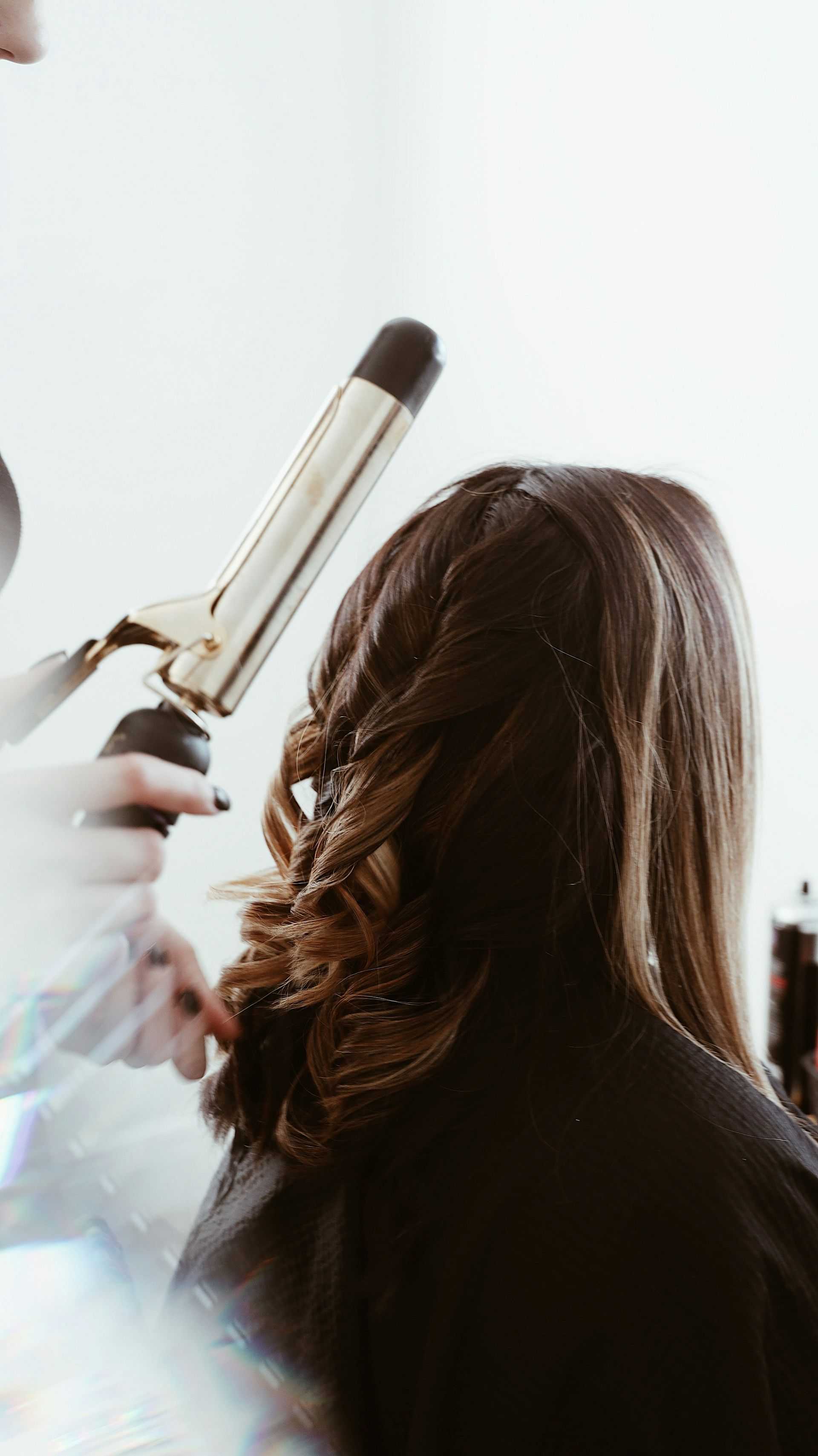 Hairdresser curling a woman's long brown hair with a curling iron.